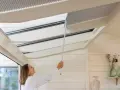 Frau befestigt mit einem Stab eine Faltgardine am Dachfenster im Wintergarten.