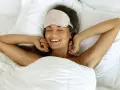 Frau mit Schlafmaske genießt den Morgen im Bett. Die Himmelsrichtung spielt keine Rolle, Hauptsache, sie ist ausgeschlafen.