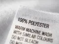 Etikett zeigt "100% POLYESTER". Dieser Stoff ist pflegeleicht und ideal für Kleidung, die oft gewaschen wird.