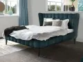 Ein luxuriöses Bett mit tiefblauem Polster und weißen Bettwäsche-Ideen. Dekorative Kissen und eine dunkle Decke laden zum Entspannen ein.
