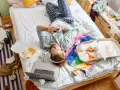 Mann liegt im Chaos auf dem Bett, umgeben von Essensresten und Kleidung. Ein typischer Tag des "bed rotting".