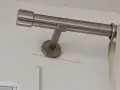 Eine Gardinenstange wird an der Wand befestigt, knapp unterhalb des Rolladenkastens. Die Halterung ist schräg montiert.
