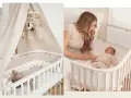 Ein Babybett neben dem Elternbett. Ein süßer Säugling schläft friedlich, während eine Mutter ihr Neugeborenes im Arm hält.