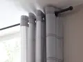 Graue Gardinen mit Karomuster hängen an einer schlichten, schwarzen Gardinenstange, die nur an den Seiten befestigt ist.