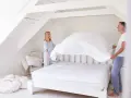 Ein Paar zieht gemeinsam ein Spannbettlaken auf. Sie lachen und scheinen Spaß daran zu haben, wie man das Spannbettlaken richtig aufzieht.