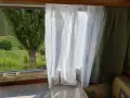 Leichte, transparente **Wohnwagen Gardinen Ideen** mit bunten Fäden vor einem Fenster mit Blick auf Weinberge.