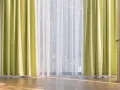 Helle, grüne Gardinen und zarter weiße Stores schmücken das Fenster. Diese Gardinen dekorieren den Raum und lassen viel Licht herein.