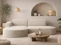 Ein gemütliches, beigefarbenes **Ecksofa mitten im Raum** lädt zum Entspannen ein. Ein runder Holztisch und ein Teppich vervollständigen das Bild.