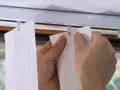 Hände befestigen einen Lamellenvorhang in einer Gardinenschiene mit Clips.