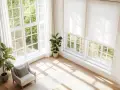 Helle Fenstergestaltung im Wohnzimmer ohne Gardinen. Sonnenschein fällt durch große Fenster auf Holzboden. Pflanzen und Sessel schaffen Gemütlichkeit.