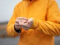Person reibt sich die Hände unter einer leuchtend orangen Jacke. Ist Polyester warm? Ja, diese Jacke hält warm.