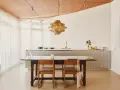 Ein Essbereich mit Holztisch und Stühlen, der den schwedischen Wohnstil verkörpert. Dahinter eine moderne Küche mit Edelstahlfronten und eine auffällige Hängelampe.