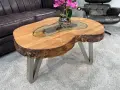 Ein Couchtisch aus massivem Holz mit Glasplatte und Metallbeinen. Die Höhe ist ideal, um Getränke und Snacks bequem zu erreichen.