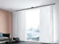 Weiße, transparente Vorhänge mit sanften Wellen und Falten rahmen ein Fenster mit Blick auf eine Stadtkulisse ein.