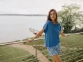 Frau auf Balkon mit Blick auf See, trägt blaues Oberteil und gemusterte Shorts. In Modal schwitzt man nicht, es ist angenehm kühl.