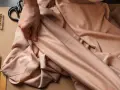 Eine Hand prüft den Fall eines fließenden Stoffes aus Viskose Polyester. Nadeln, Schere und Garn liegen bereit.