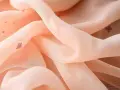 Zartes, pfirsichfarbenes Mesh-Textil mit kleinen, roten Herzchen-Mustern, das sanft fällt und glänzt.
