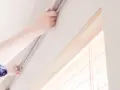 Hände befestigen eine Gardinenschiene an der Decke ohne Bohren. Einfache Montage für Ihre Fensterdekoration.