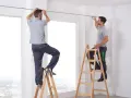 Zwei Männer auf Leitern bringen eine Gardinenschiene an.