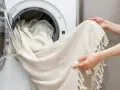 Helle Gardinen werden in die Waschmaschine geladen. Mit Backpulver werden sie wieder strahlend weiß.