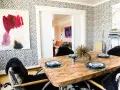 Esszimmer mit auffälliger Tapete im Jaguar Muster. Ein Holztisch mit Tellern und ein Kunstwerk an der Wand.