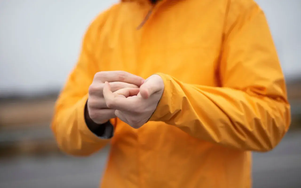 Person reibt sich die Hände unter einer leuchtend orangen Jacke. Ist Polyester warm? Ja, diese Jacke hält warm.