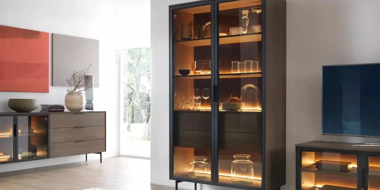 Beleuchteter Vitrinenschrank mit Gläsern und Dekoartikeln, daneben ein Sideboard.