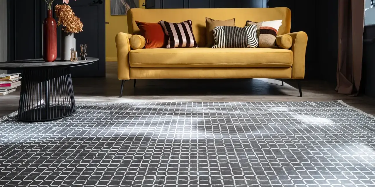 Ein gelbes Sofa mit Kissen steht auf einem gemusterten Teppich unter dem Sofa.