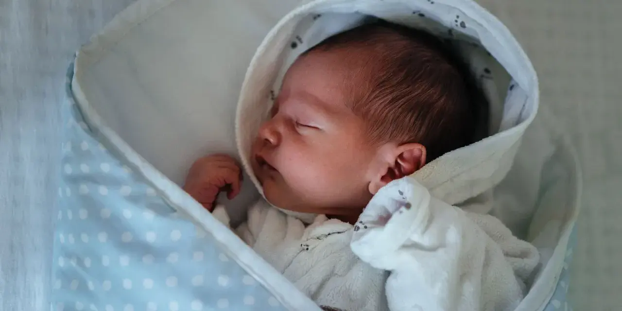 Neugeborenes Baby schläft friedlich, eingewickelt in eine Decke. Der sanfte "white noise" des Geräuschs hilft ihm beim Einschlafen.