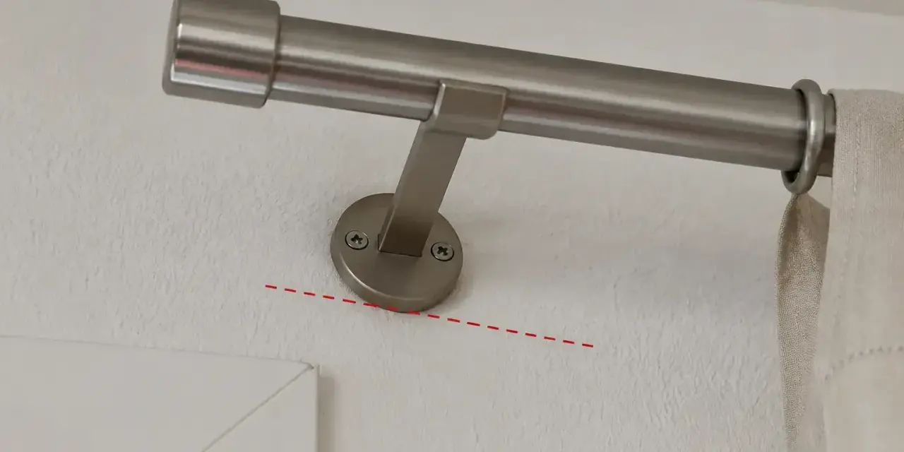 Eine Gardinenstange wird an der Wand befestigt, knapp unterhalb des Rolladenkastens. Die Halterung ist schräg montiert.