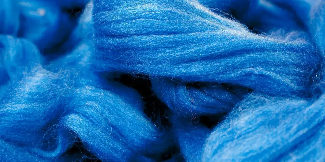 Leuchtend blaue Fasern, die an Wolle erinnern. Obwohl sie sich wie eine Naturfaser anfühlt, ist Viskose eine künstlich hergestellte Faser.