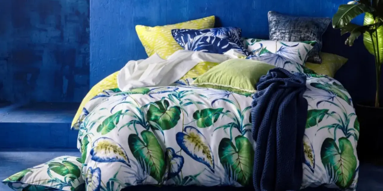 Ein tropisch gemustertes Bett mit Kissen in Blau und Grün. Für ein frisches Gefühl: wie oft Bettdecke wechseln?