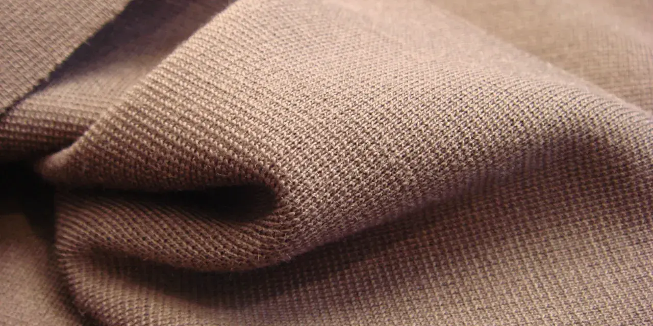 Braune Stofffalten, die die glatte, feine Struktur von Single Jersey zeigen. Dieses Material ist weich und dehnbar.