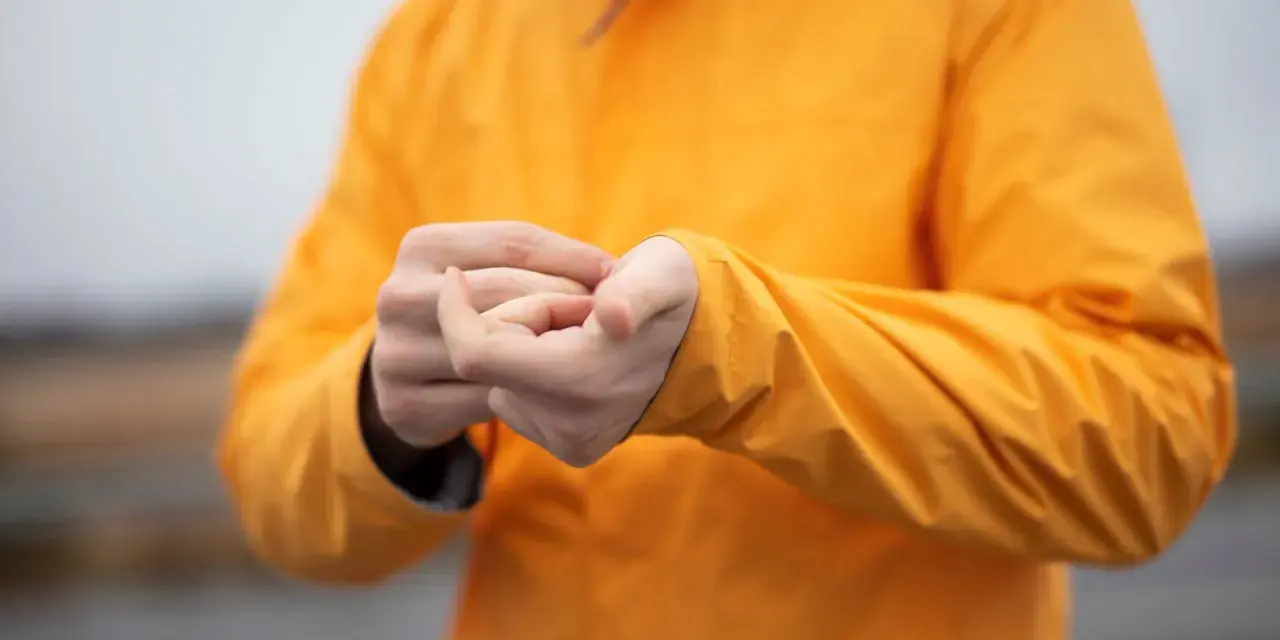 Person reibt sich die Hände unter einer leuchtend orangen Jacke. Ist Polyester warm? Ja, diese Jacke hält warm.