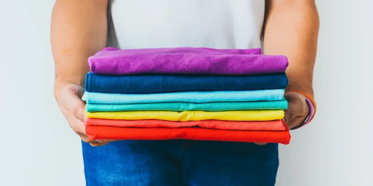Ein Stapel bunter GSM Kleidung, gehalten von Händen in Jeans.