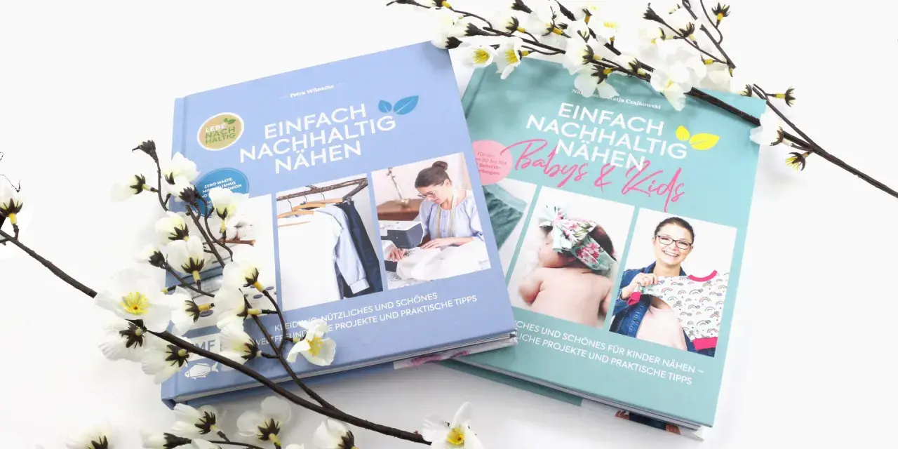 Zwei Bücher über nachhaltiges Nähen mit umweltfreundlichen Stoffen, umgeben von blühenden Zweigen.