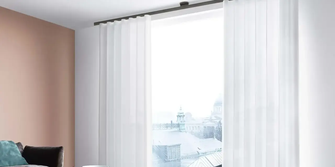 Weiße, transparente Vorhänge mit sanften Wellen und Falten rahmen ein Fenster mit Blick auf eine Stadtkulisse ein.