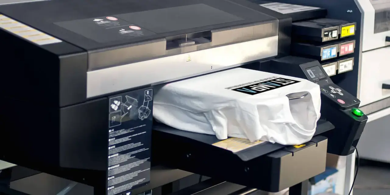 Moderne Maschine für den **digitaldruck textil**. Eine weiße T-Shirt wird bedruckt mit schwarzem Text.
