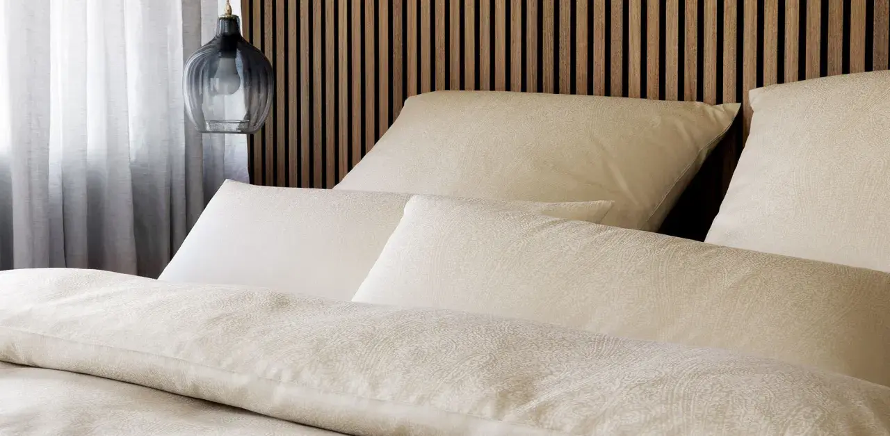 Gemütliches Bett mit Kissen und Decken im dezenten **muster paisley**. Ein moderner Nachttischlampen-Pendel hängt daneben.