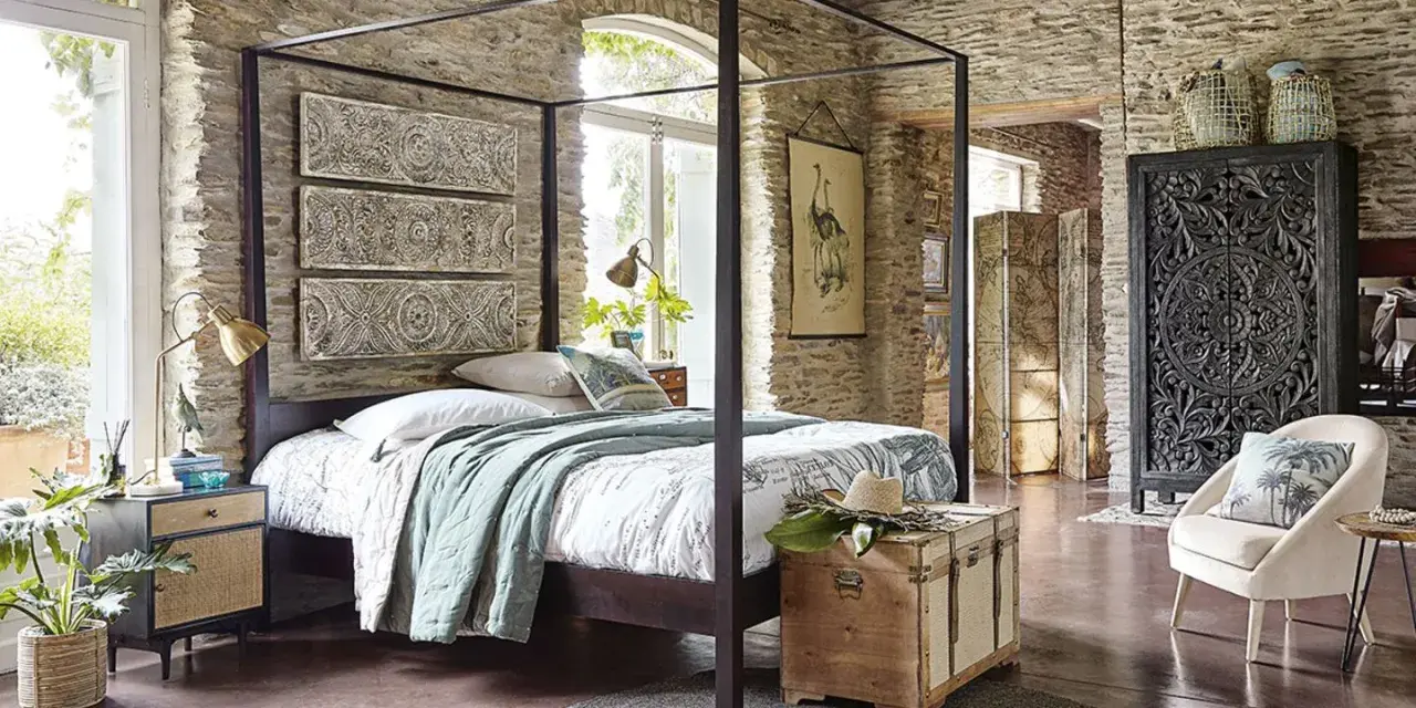 Ein Schlafzimmer mit Steinwänden und einem Himmelbett. Drei Wandpaneele mit orientalischen Mustern hängen über dem Bett. Ein Holztruhe steht am Fußende.