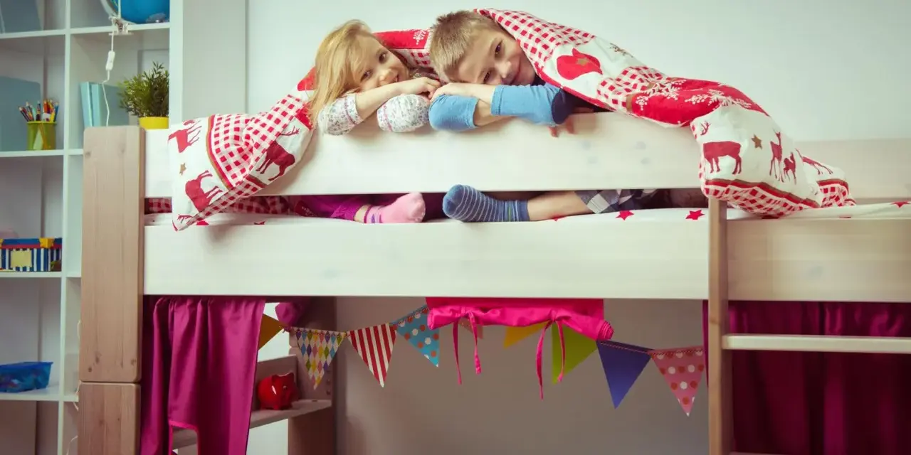 Zwei Kinder kuscheln sich unter einer Decke auf einem Hochbett. Die Frage "Hochbett ab wann?" stellt sich hier nicht, die Kleinen sind begeistert!