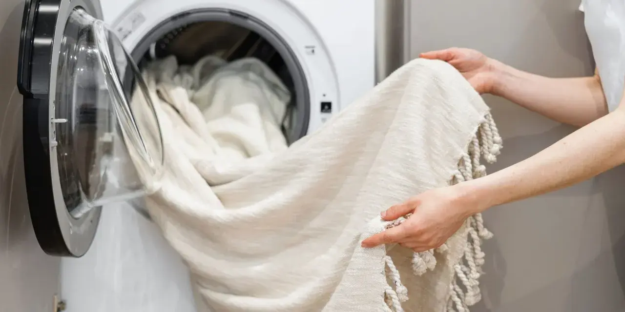 Helle Gardinen werden in die Waschmaschine geladen. Mit Backpulver werden sie wieder strahlend weiß.