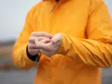 Person reibt sich die Hände unter einer leuchtend orangen Jacke. Ist Polyester warm? Ja, diese Jacke hält warm.