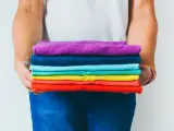 Ein Stapel bunter GSM Kleidung, gehalten von Händen in Jeans.