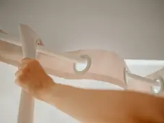 Eine Hand zieht einen hellrosa Vorhang mit Ösen über eine weiße Stange. Zeit für die Gardinen zu waschen!