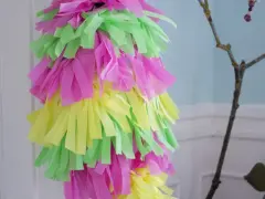 Bunte Papierstreifen in Pink, Gelb und Grün hängen von einem Ast. Ein selbstgemachtes **Pinata basteln**-Projekt für eine fröhliche Feier.