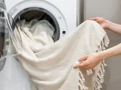 Helle Gardinen werden in die Waschmaschine geladen. Mit Backpulver werden sie wieder strahlend weiß.
