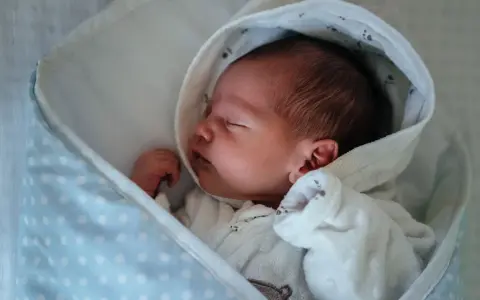 Neugeborenes Baby schläft friedlich, eingewickelt in eine Decke. Der sanfte "white noise" des Geräuschs hilft ihm beim Einschlafen.