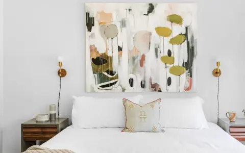 Modernes Schlafzimmer renovieren: Weißes Bett mit Kissen, Nachttisch und abstraktem Gemälde über dem Kopfende.