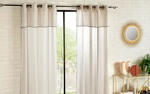 Helle Gardinen mit schwarzer Umrandung sind hochgesteckt und rahmen ein Fenster mit Blick ins Grüne ein.